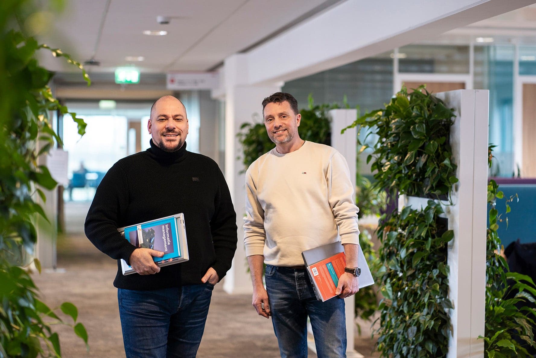 2 studenten lopen door het schoolgebouw met een laptop en boek in hun handen