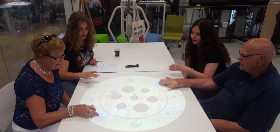 2 studenten en 2 ouderen spelen een spel dat op tafel wordt geprojecteerd