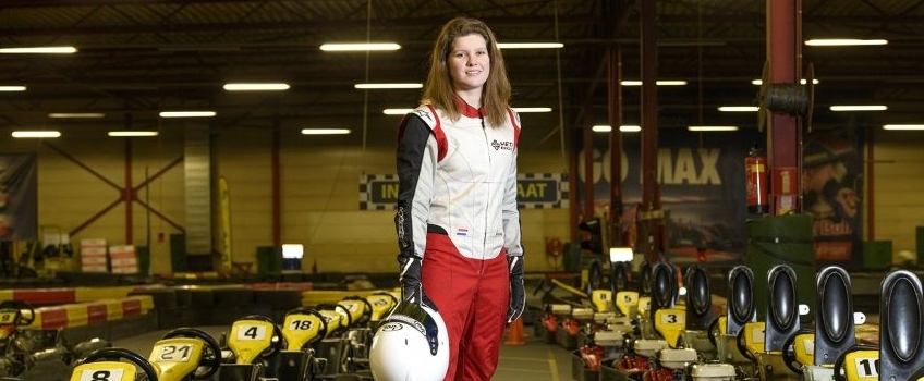 Anne poseert in racepak met helm tussen karts