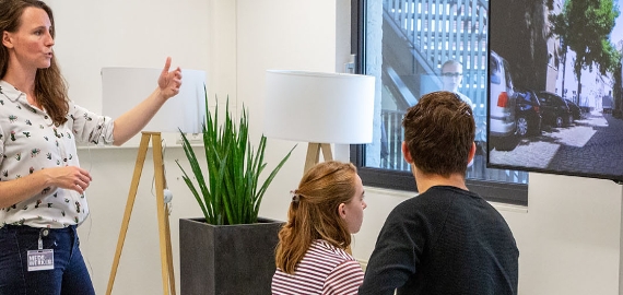 studente op hometrainer gekoppeld aan scherm, docent geeft uitleg